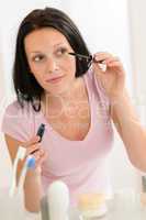 Woman apply mascara in front bathroom mirror