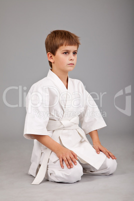Karate boy in white kimono is sitting