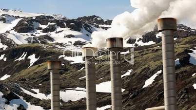 Steam rising from a geothermal electrical company in Iceland with snowcovered mountains in the background.