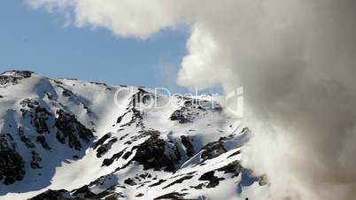 Steam rising from a geothermal electrical company in Iceland with snowcovered mountains in the background.