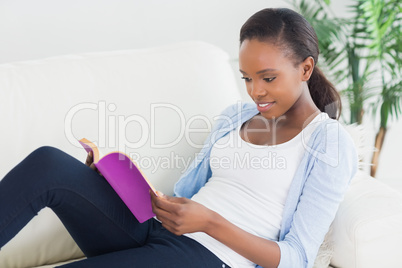 Black woman sitting on a sofa while reading a book