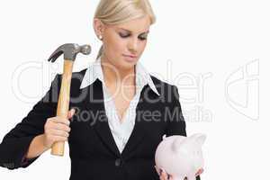 Serious businesswoman holding a piggy-bank and hammer