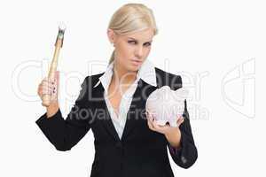 Serious businesswoman holding a hammer and a piggy-bank