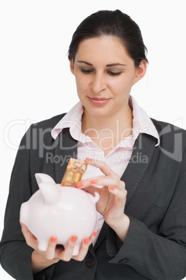 Brunette businesswoman putting money into a piggy-bank