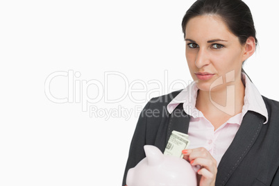 Brunette businesswoman putting dollars into a piggy-bank