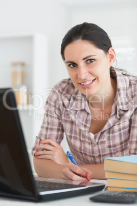 Smiling woman writing on notebook beside laptop Smiling woman writing on notebook beside laptop