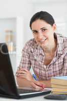 Smiling woman writing on notebook beside laptop