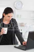 Woman looking at a laptop while holding a mug