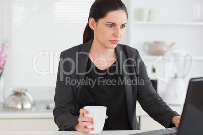 Woman holding a mug while looking at a laptop