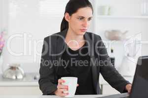 Woman holding a mug while looking at a laptop