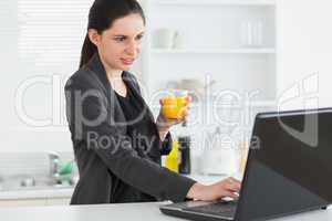 Woman looking at a laptop while holding a juice glass