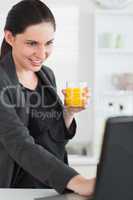 Woman holding a juice glass while looking at a laptop