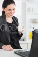 Woman holding a milk glass while looking at a laptop