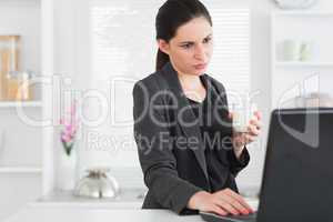 Woman looking at a laptop while holding a milk glass