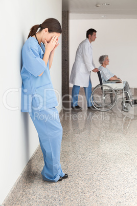 Stressed nurse leaning against wall