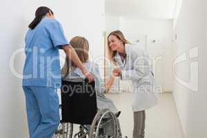Doctor talking to patient in wheelchair while nurse is pushing