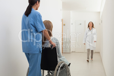 Nurse pushing patient in wheelchair with doctor approaching