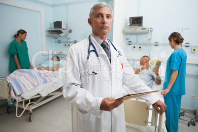 Doctor with clipboard in busy hospital room