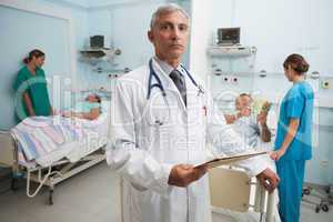 Doctor with clipboard in busy hospital room