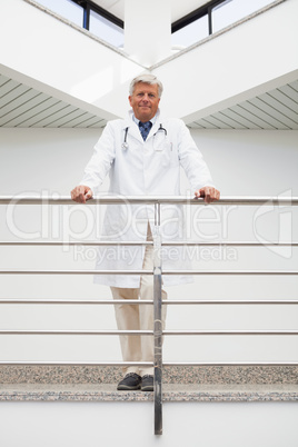 Smiling doctor leaning against rail