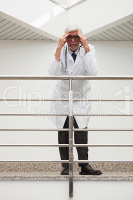 Stressed doctor  leaning on  railing with hands on forehead in h