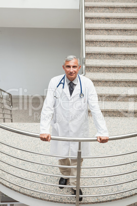 Smiling doctor leaning on  the railing of the stairs