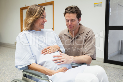 Pregnant woman and partner both touching her belly and smiling