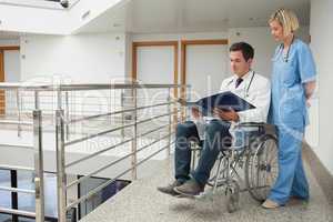 Doctor sitting in wheelchair examining notes with nurse