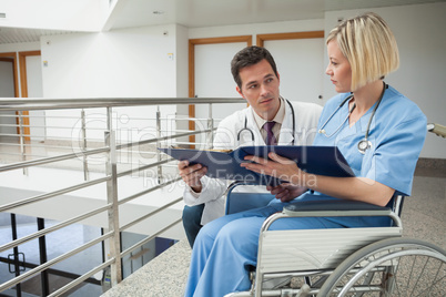 Doctor and nurse in wheelchair studying folder