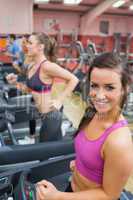 Women running on a treadmill in a gym smiling