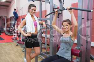 Woman stands beside friend using weights machine