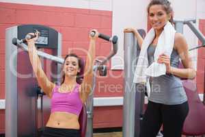 Woman stands beside other woman using weight machine