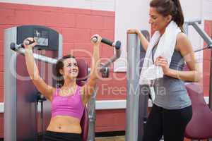 Women using weight machine smiling at friend