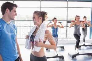 Aerobics class lifting weights while woman talking to trainer
