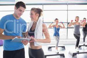 Trainer presenting timetable while aerobics class lifting weight