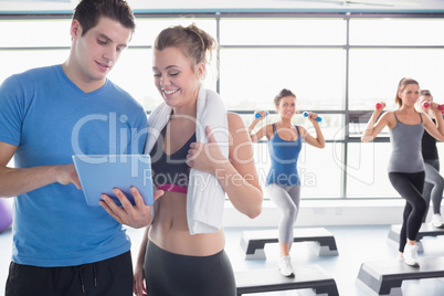 Trainer and woman talking while aerobics class lifiting weights