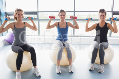 Three smiling women sitting on exercise balls and lifting weight