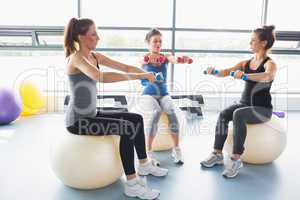 Three women lifting weights together on exercise balls