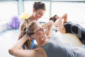 Female trainer helping woman doing sit-ups