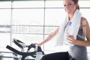 Woman holding a bottle and riding a exercise bike