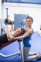 Happy woman lifting weights and her trainer