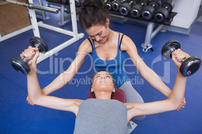 Cheerful trainer helping woman lifting weights