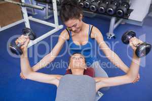 Cheerful trainer helping woman lifting weights