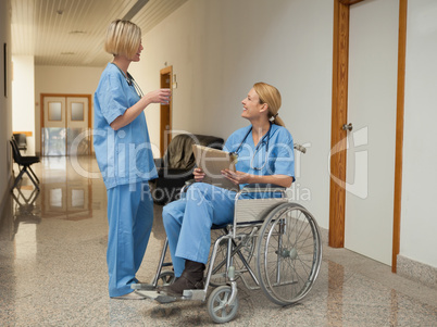 Nurse with drink talking to nurse in wheelchair with folder