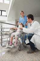 Doctor crouching next to child in wheelchair with nurse pushing
