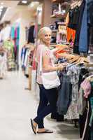 Woman standing in a shop looking for clothes smiling