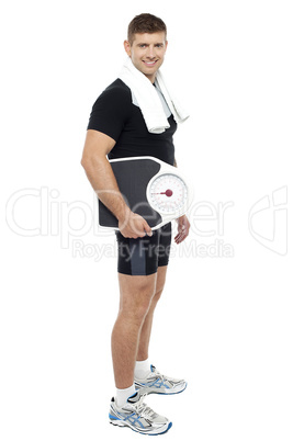 Full length portrait of young male carrying weight scale