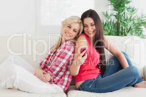 Women sitting back to back smiling and lookig at phone