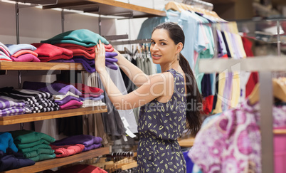 Woman putting jumpers on shelf