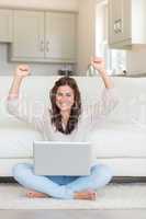Successful woman raising her hands in front of laptop